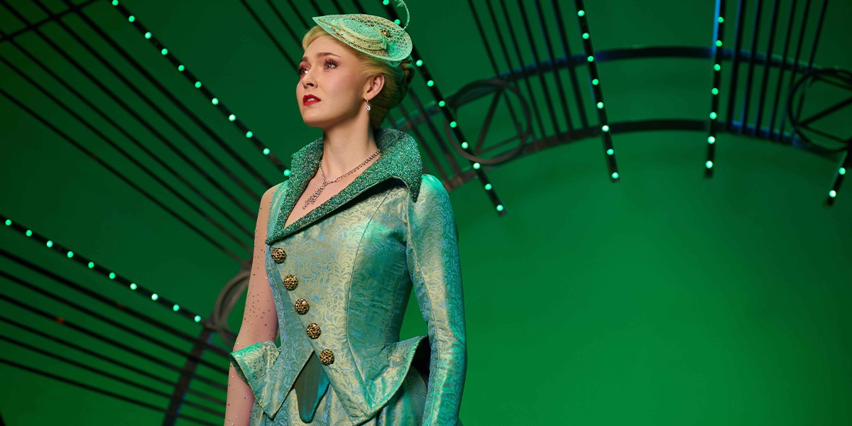 A vibrant stage scene from "Wicked," featuring actors in elaborate costumes against a dramatic backdrop.