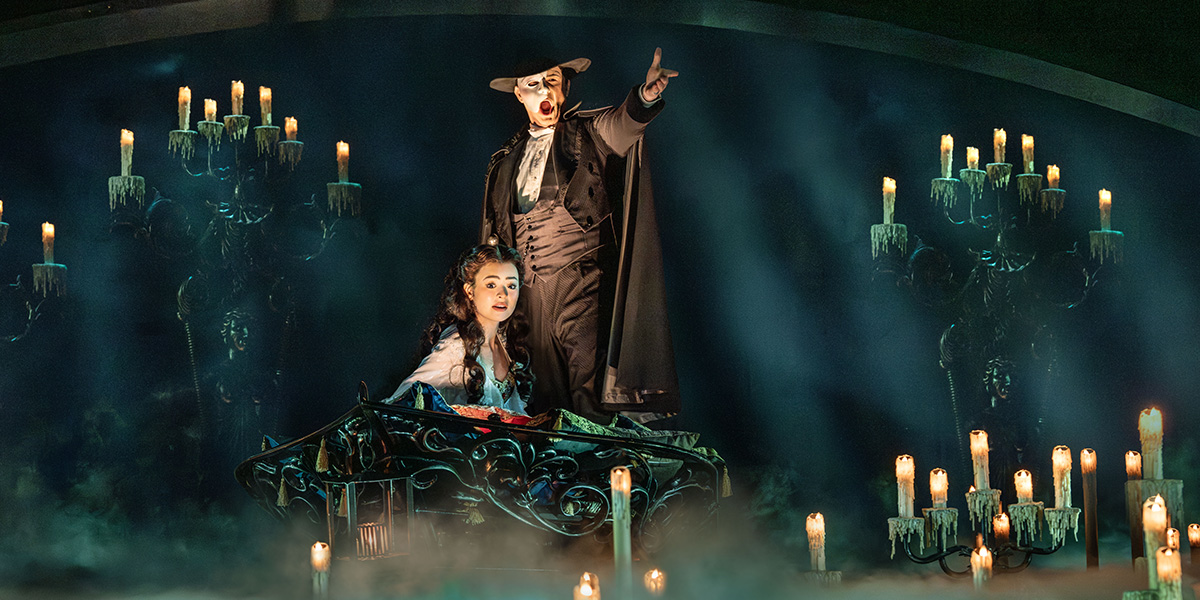 Anna Zavelson as Christine and Dean Chisnall as The Phantom, in dramatic poses, with theatrical lighting.