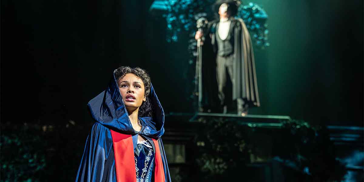 Beatrice Penny-Touré gazes upwards, wearing a blue cloak, while a figure in a cape looms above.