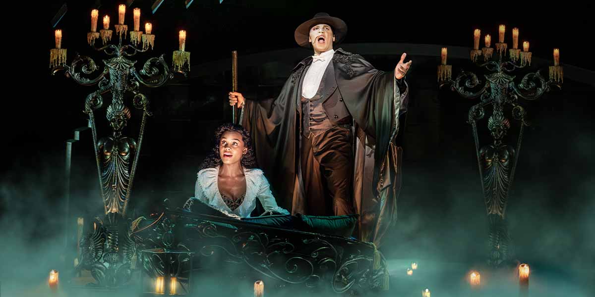 Jordan Donica, in a dark cloak, sings passionately beside Beatrice Penny Touré, seated in a misty, candlelit setting.