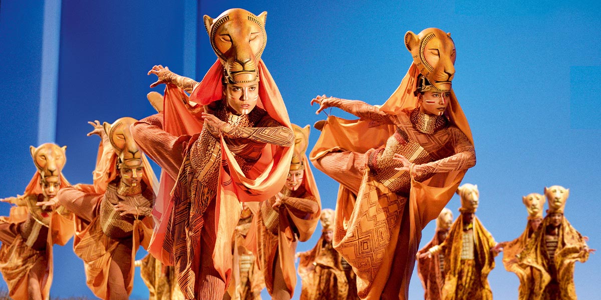 A lioness crouches in tall grass, poised to hunt, with a blurred savannah background.