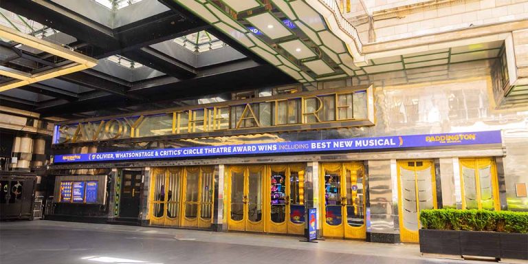The Savoy Theatre exterior features ornate architecture, with a marquee displaying the theatre's name and bright lights.
