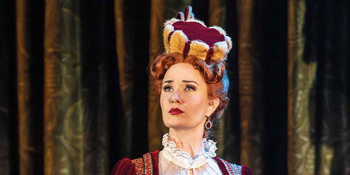 Sierra Boggess as Carlotta, wearing a crown, gazes thoughtfully with red hair and elegant costume.