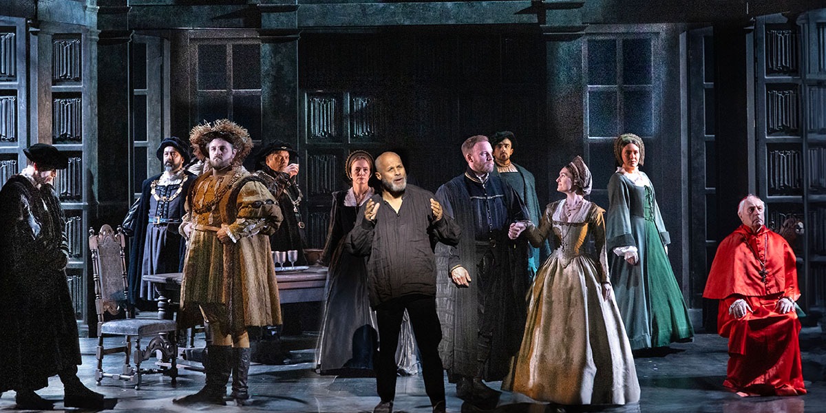 11 actors standing on stage in a variety of poses, in Tudor dress