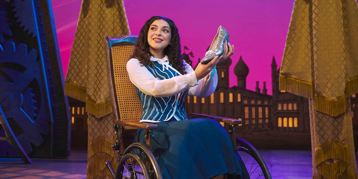 Hannah Qureshi performing on stage in a green costume, with dramatic lighting and a dark background.