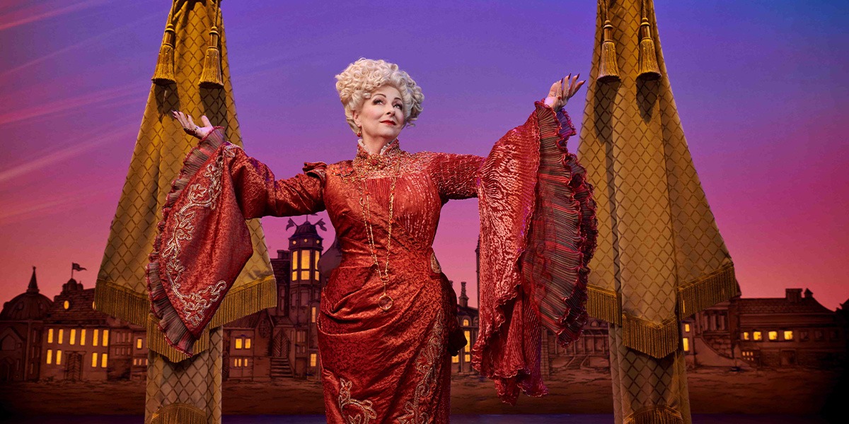 A woman in a green dress stands on stage, with a dark curtain and spotlight in the background.