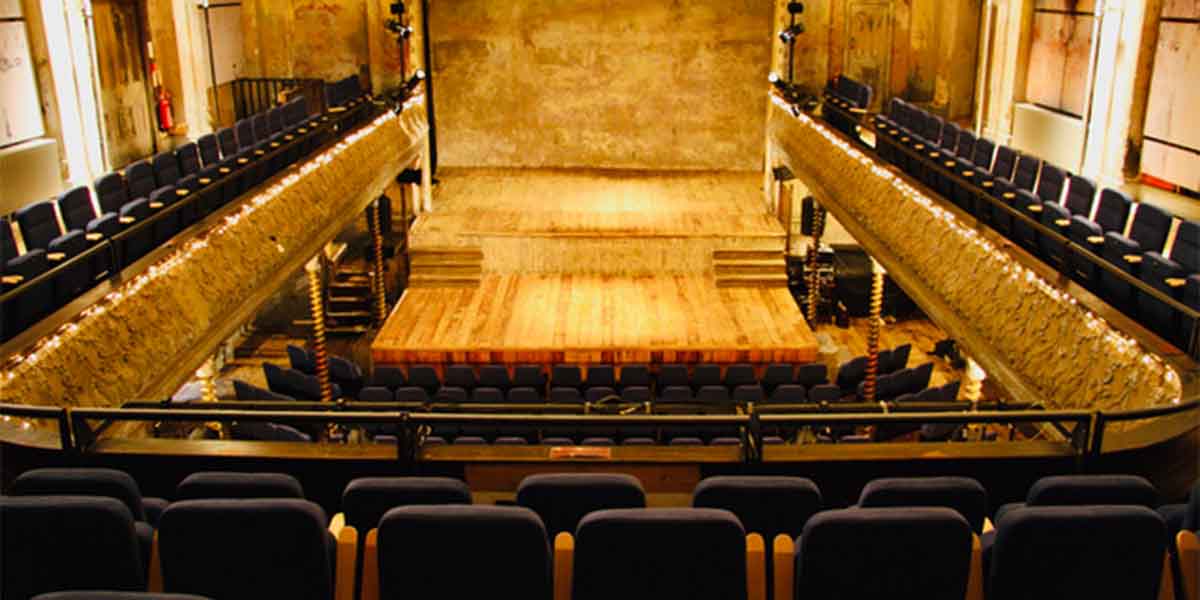 Interior of Wilton's Music Hall, featuring wooden flooring, tiered seating, and textured walls.