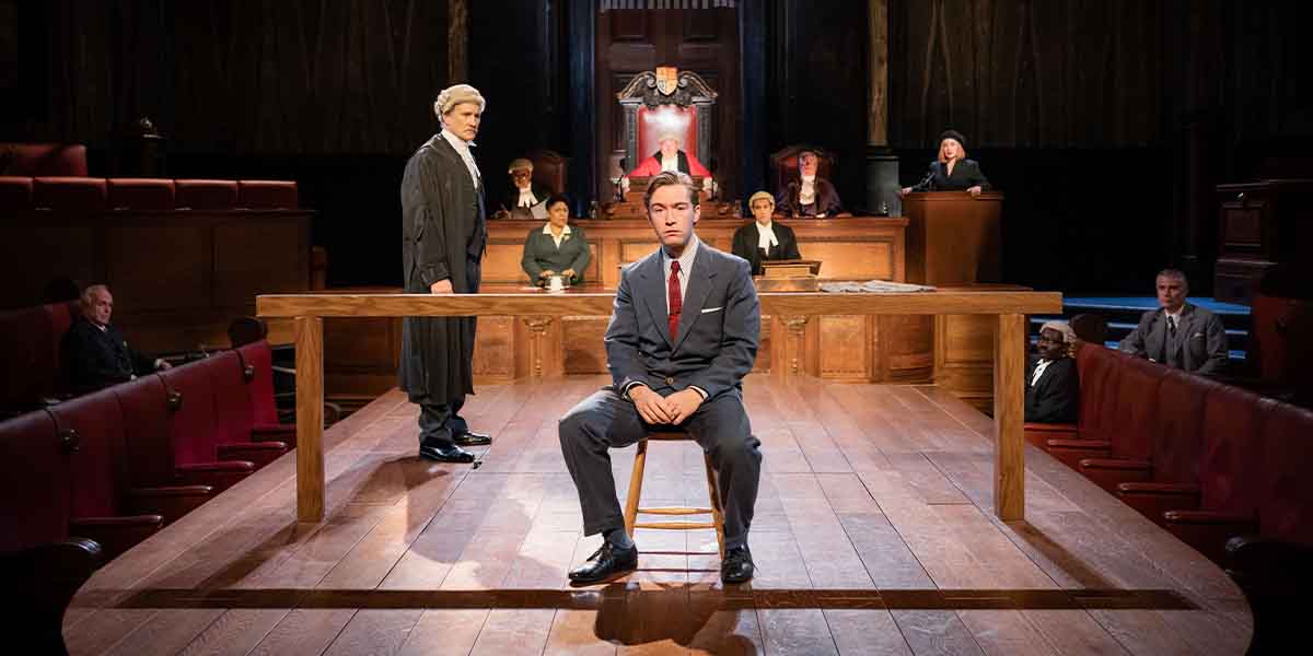 A courtroom scene from "Witness for the Prosecution," featuring a seated man and a standing lawyer.