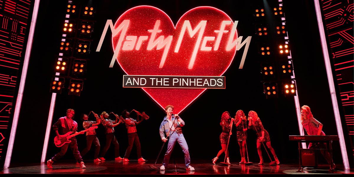 Caden Brauch as Marty McFly stands centre stage with cast members, vibrant costumes, and dynamic lighting.