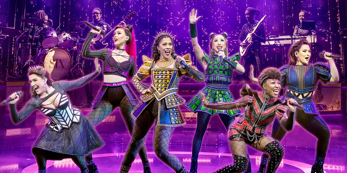 The cast of SIX the Musical performs on stage, wearing vibrant costumes with dynamic poses and expressive gestures.