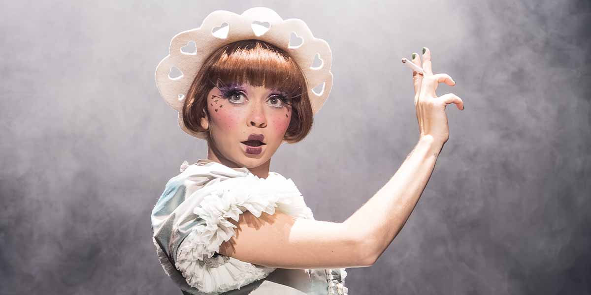 Sarah Hyland as Sally Bowles, wearing a white hat and frilly costume, striking a dramatic pose.