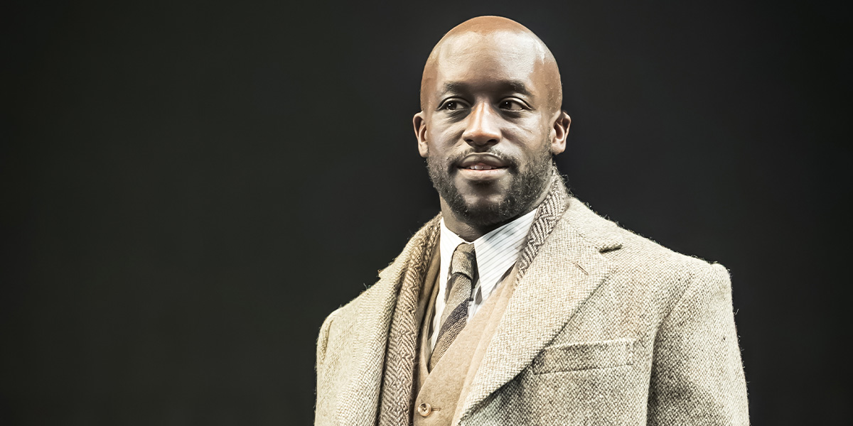 A performer in a sequined costume poses dramatically on stage, with vibrant lighting and a dark background.