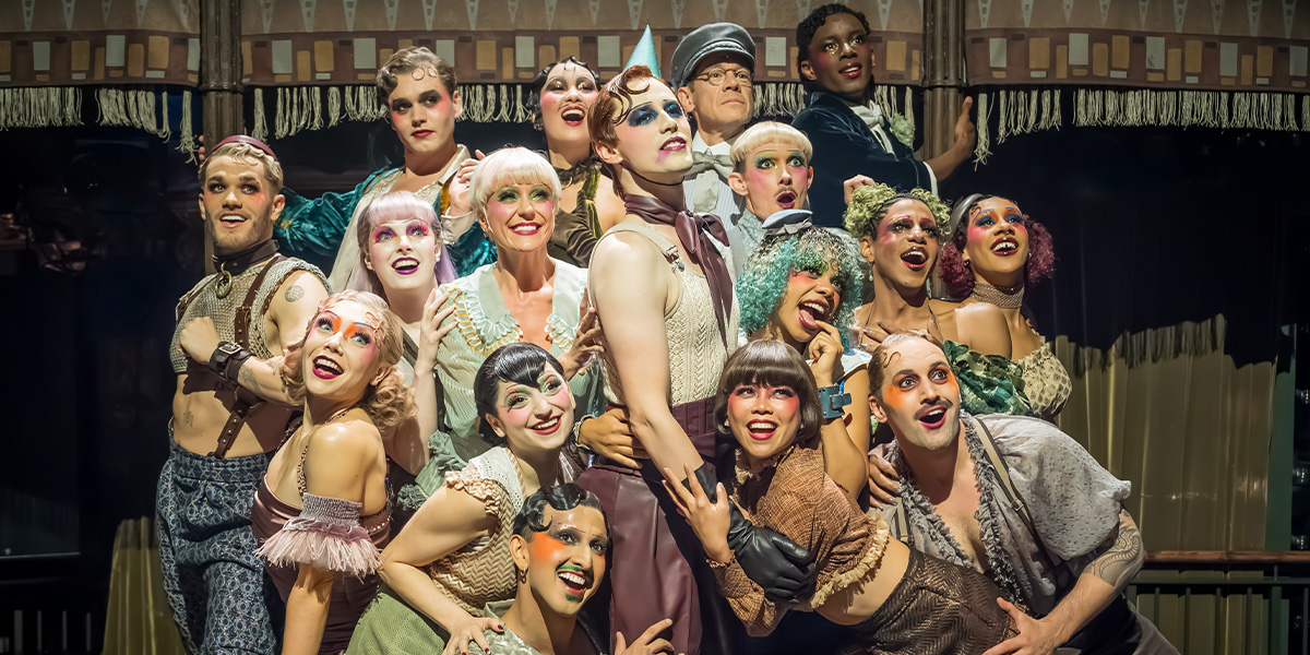 A performer in a sequined costume poses dramatically on stage, with vibrant stage lights illuminating the scene.