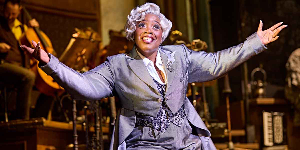 Malinda Parris performs joyfully in a grey suit, with a bright smile, against a musical backdrop.