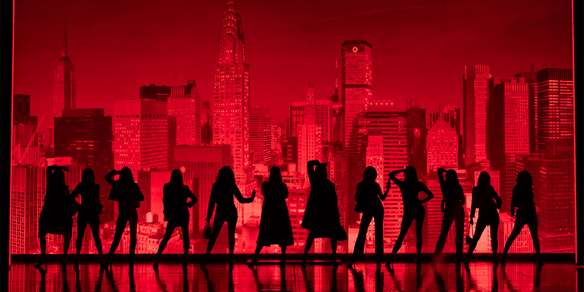 The cast of The Devil Wears Prada poses together, dressed in stylish outfits against a neutral backdrop.