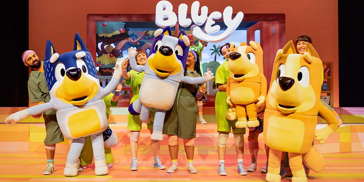 Characters in colourful costumes celebrate on stage, with a large "BLUEY" sign above them.