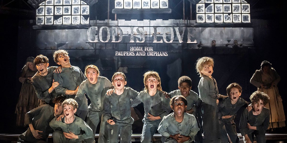 A performer in a bright costume poses dramatically on stage, with colourful lighting and a vibrant backdrop.