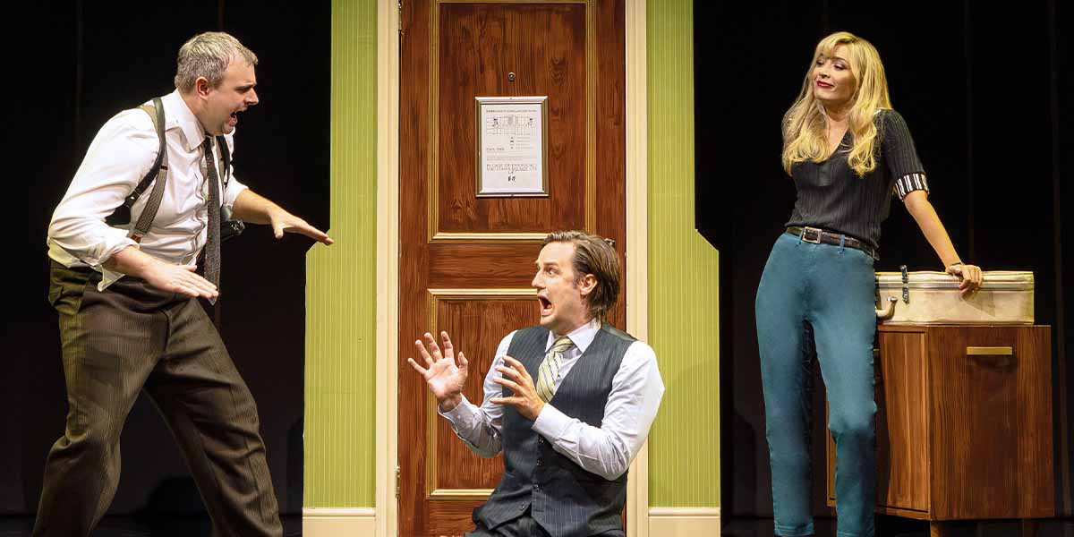 Chris Leask and Henry Shields express surprise, while Bryony Corrigan stands calmly beside a wooden cabinet.