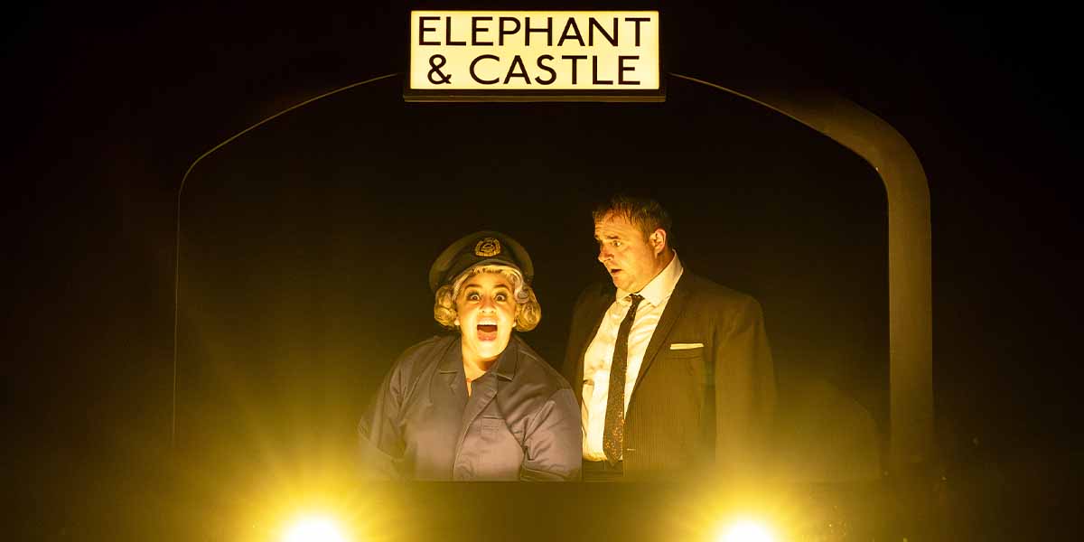 Nancy Zamit, in a police uniform, dramatically reacts beside Chris Leask, under an illuminated sign reading "ELEPHANT & CASTLE.