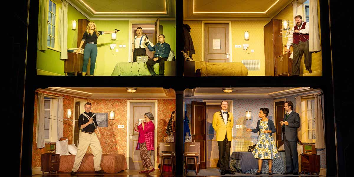 The cast of "The Comedy About Spies" poses together in hotel room setting, smiling and dressed in casual attire.