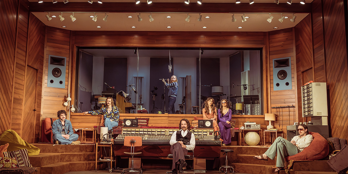 A musician plays a guitar on stage, surrounded by colourful lights and an engaged audience in the background.