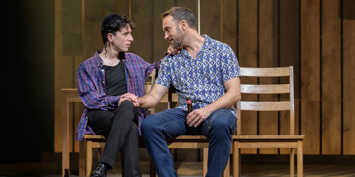 Two people are sitting together. The person on the right has one hand on the others knee.