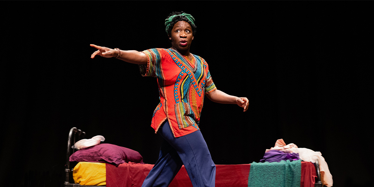 Apphia Campbell performs energetically in a colourful patterned top, gesturing towards the audience on stage.