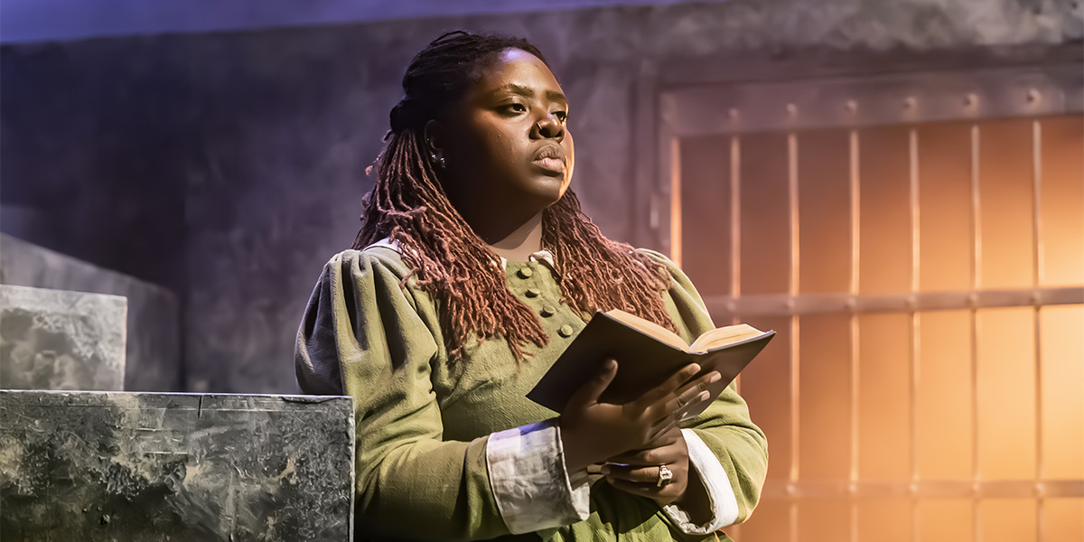 Shiloh Coke as Frances stands centre stage in Coven, wearing a dark costume against a dramatic backdrop.