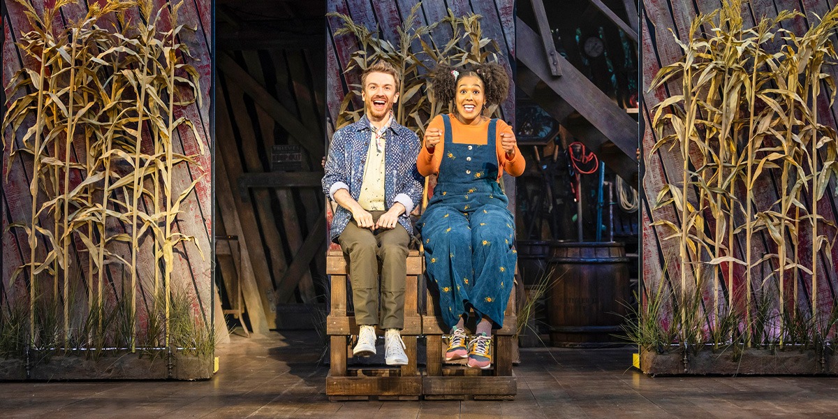 Steven Webb (Storyteller 2) and Monique Ashe-Palmer as (Storyteller 1) are sitting on stage and look to be driving a vehicle.
