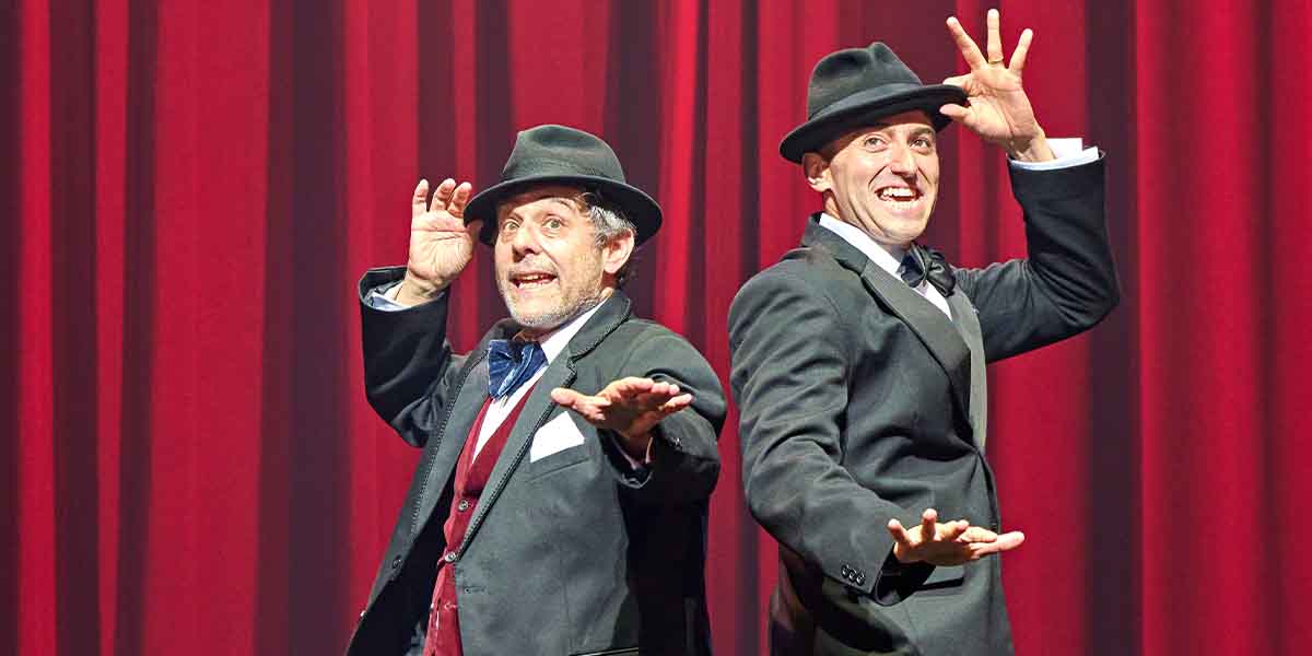 Andy Nyman as Max Bialystock and Marc Antolin as Leo Bloom pose playfully in front of red curtains.