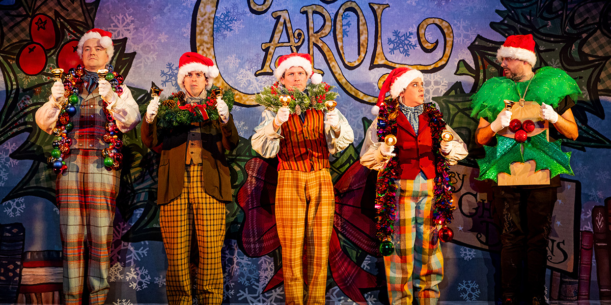 A group of actors from "Christmas Carol Goes Wrong" poses together, wearing festive costumes and smiling.