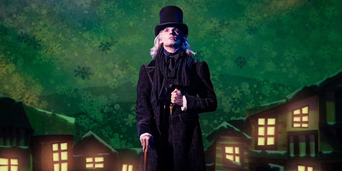 Daniel Fraser performing in a festive costume, smiling, with Christmas decorations in the background.