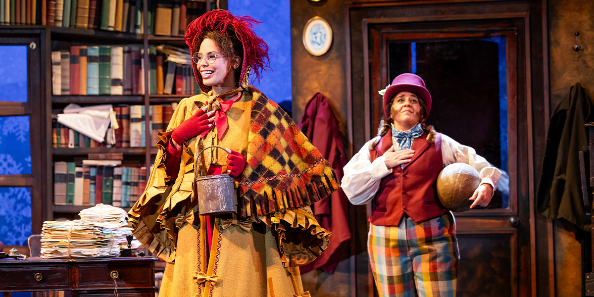 Sasha Frost and Nancy Zamit pose together, smiling, in festive costumes with holiday decorations in the background.
