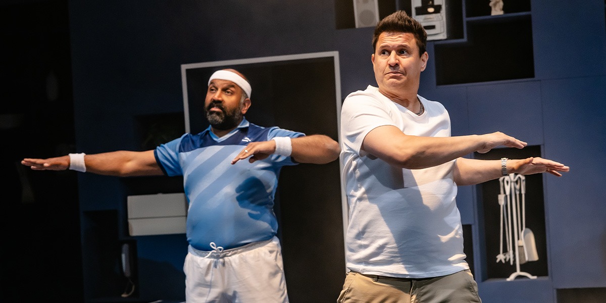 Two actors performing in a modern setting, one in a blue sports top and the other in white.
