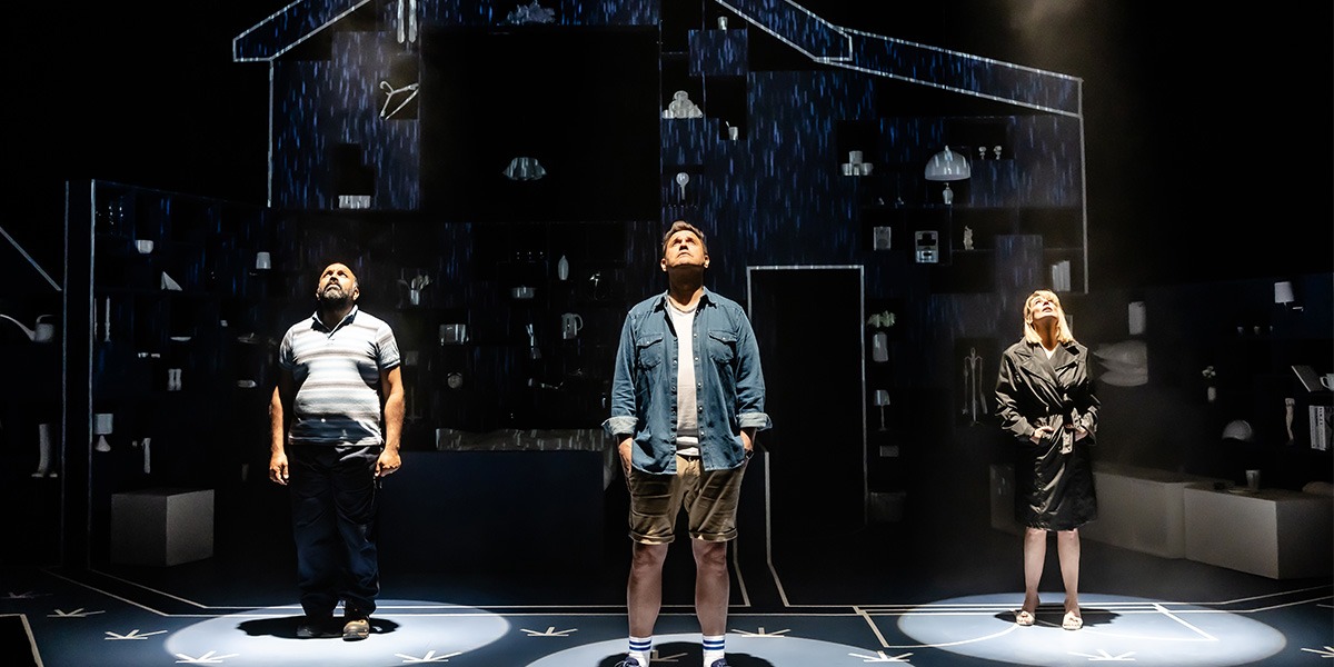 Three actors are on stage in a dramatic lighting, looking upwards, in a scene featuring a detailed set with digital rain and diverse lighting effects.