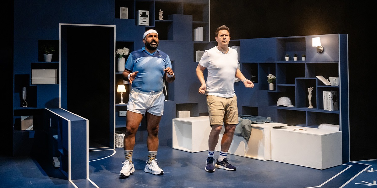 Two actors are on stage, they are dressed in casual attire, both look to be exercising.