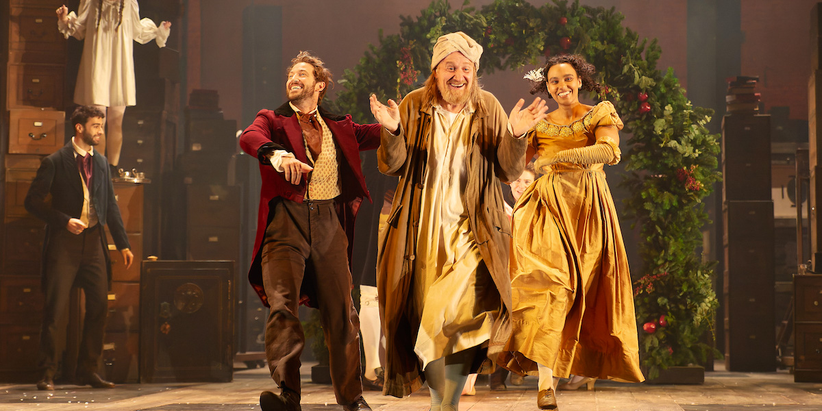 A scene from A Christmas Carol at Alexandra Palace, featuring actors in Victorian costumes on stage dancing.