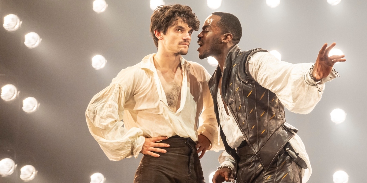 Edward Bleumel and Ncuti Gatwa pose together, smiling, against a soft-focus background with warm lighting.