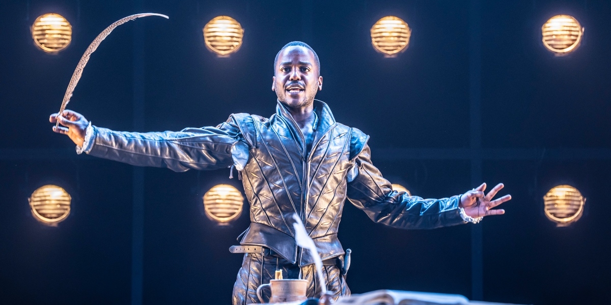 Ncuti Gatwa poses confidently, wearing a patterned shirt, with a soft-focus background and warm lighting.