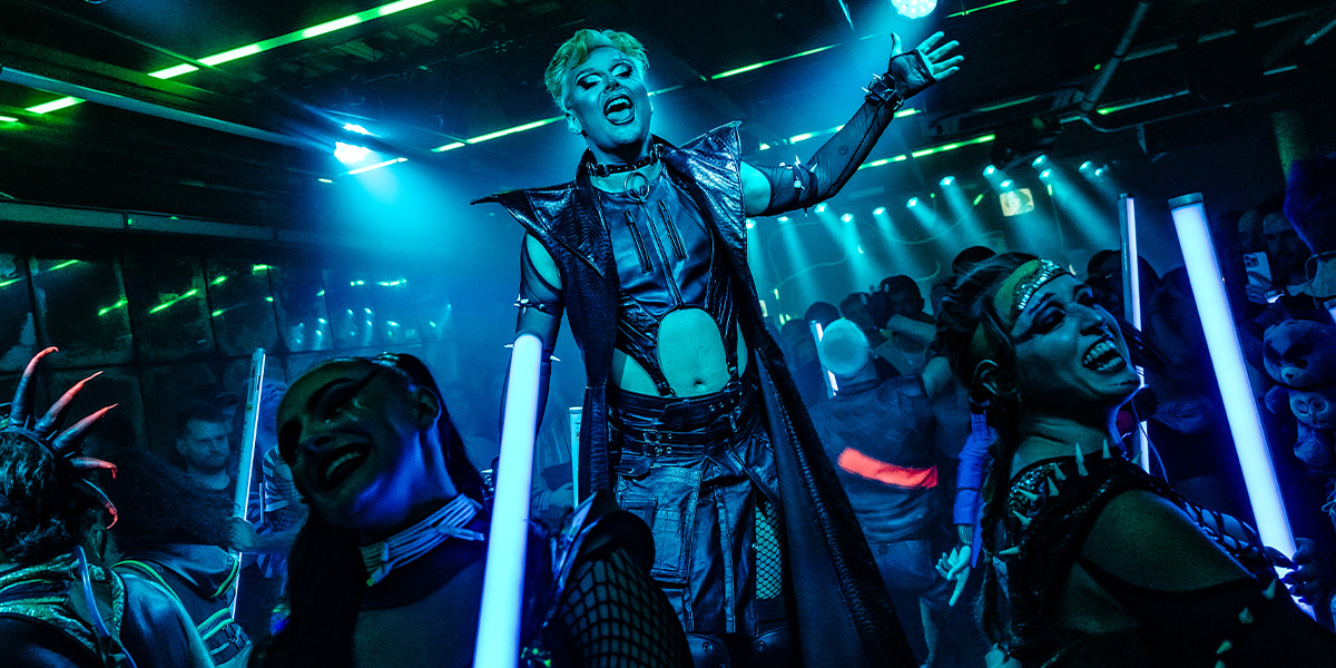 Jan Sport, dressed as Oscar Wilde, poses in a lavishly decorated room with ornate furnishings.