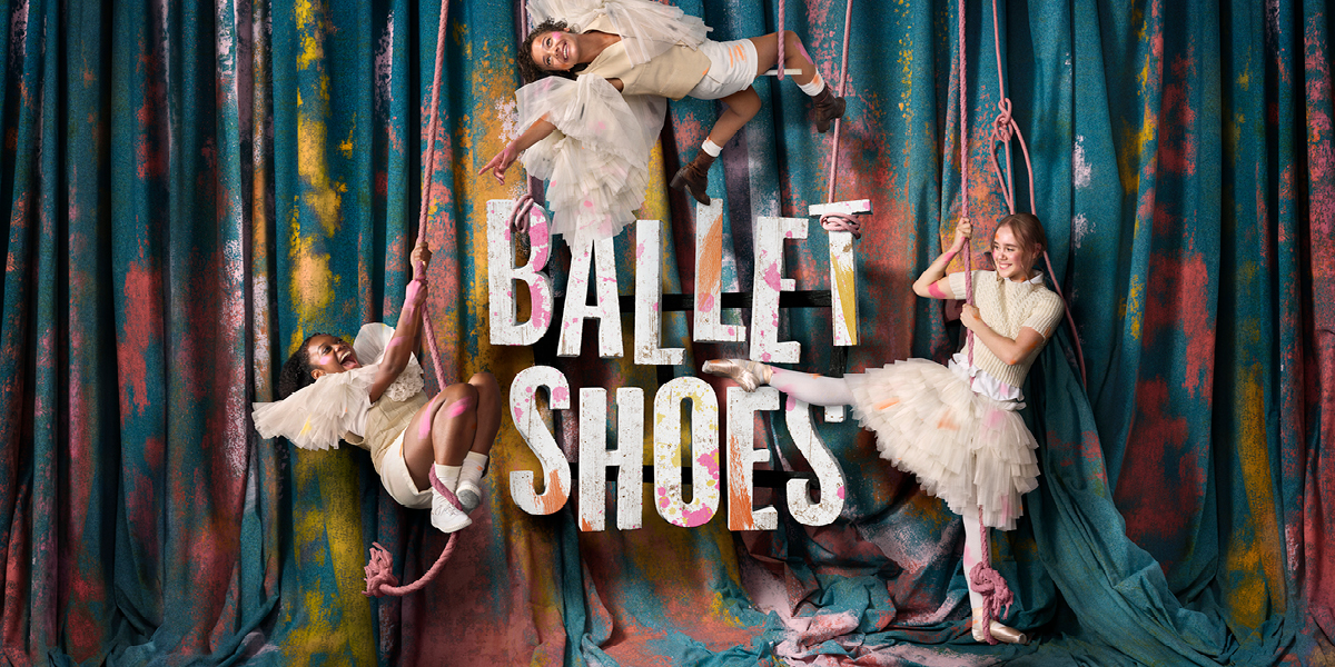 A pair of pink ballet shoes with ribbons, placed on a wooden floor, surrounded by soft lighting.