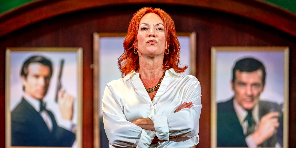 Person with crossed arms standing in front of two framed portraits of James Bond, depicted by Roger Moore.