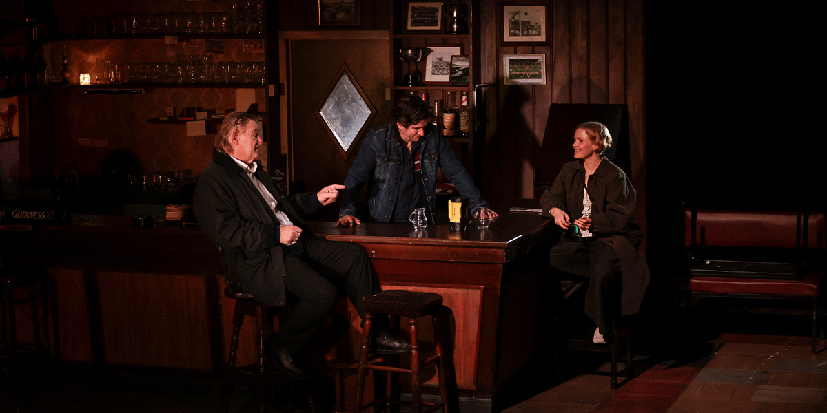 Brendan Gleeson and Jack Owen McDonnell sit on a sofa, while Kate Phillips and Valerie stand nearby, engaged in conversation.