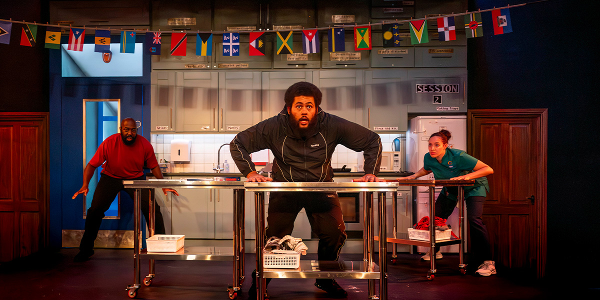 Five individuals stand together outdoors, smiling. They wear casual clothing, with greenery in the background.