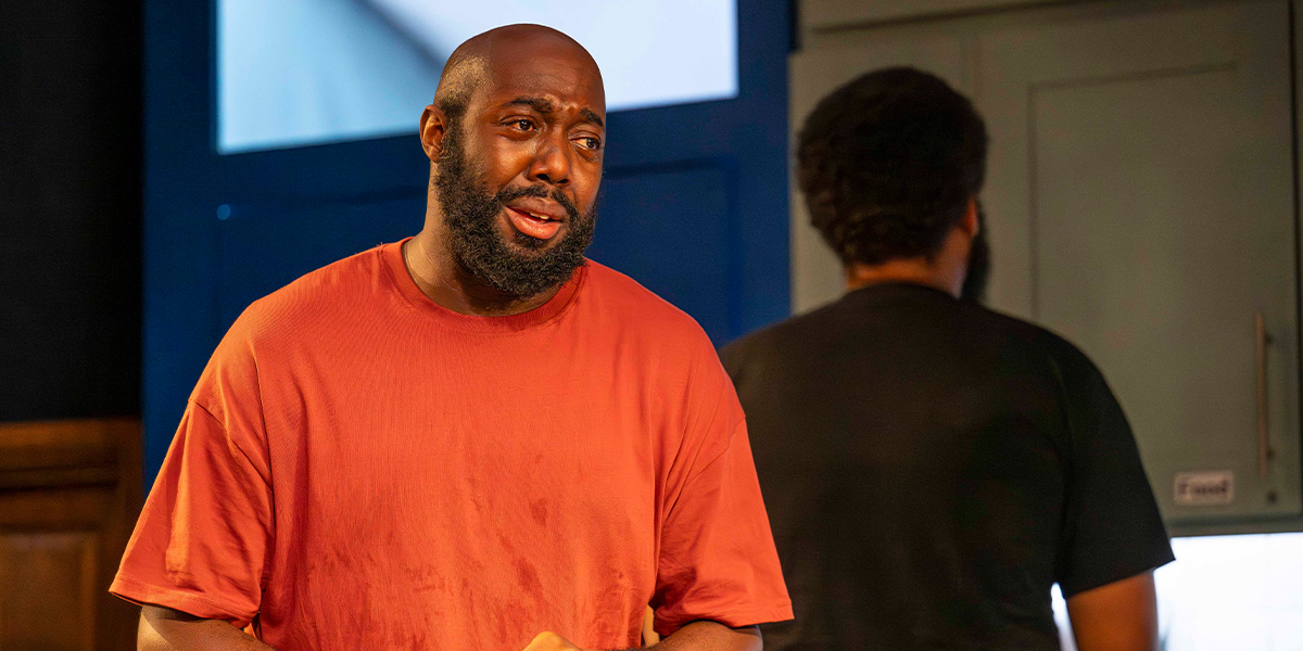 Two men sit at a table, engaged in conversation, with warm lighting and a wooden background.