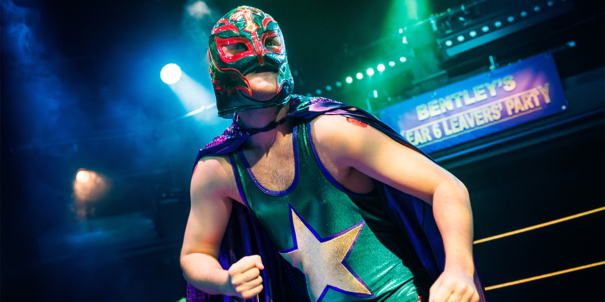 A group of diverse individuals poses together, smiling, in a brightly lit indoor setting with colourful decorations.