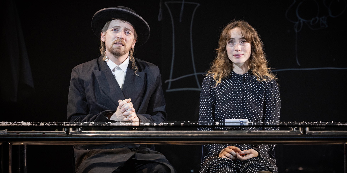 Eddie Toll as Schmuli and Katerina Tannenbaum as Esther interact on stage, dressed in period costumes.
