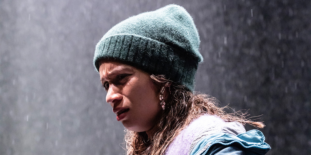 Isobel Akuwudike stands on a rocky shore, wearing a flowing blue dress, gazing thoughtfully at the sea.