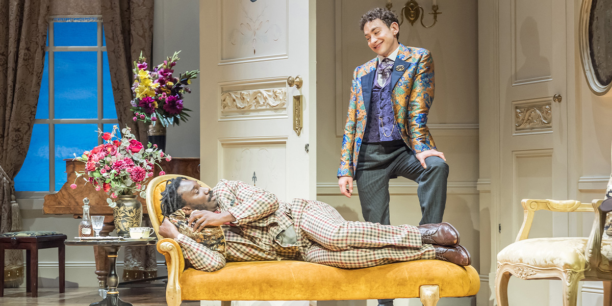 Nathan Stewart-Jarrett and Olly Alexander pose together on stage, dressed in period costumes, with dramatic lighting.
