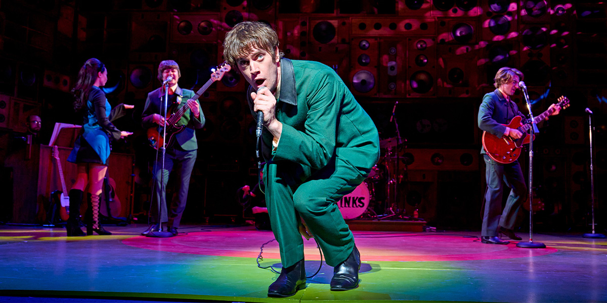 A group of performers in vibrant costumes, energetically singing and dancing on a brightly lit stage.